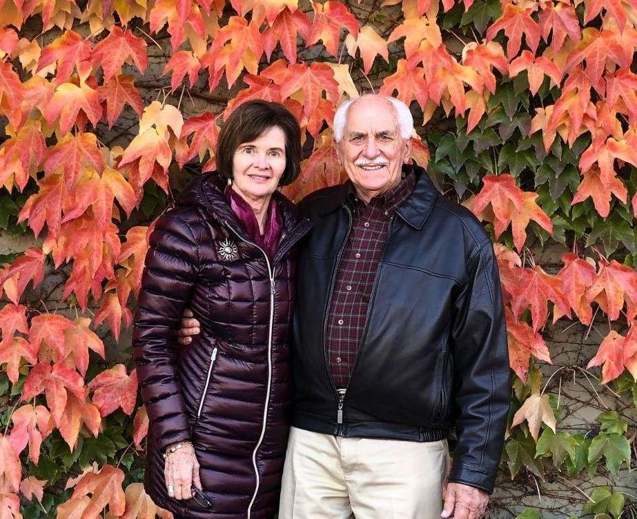 Roy and Suzanne Miller stand outside in front of vibrant red, orange, and yellow foliage.