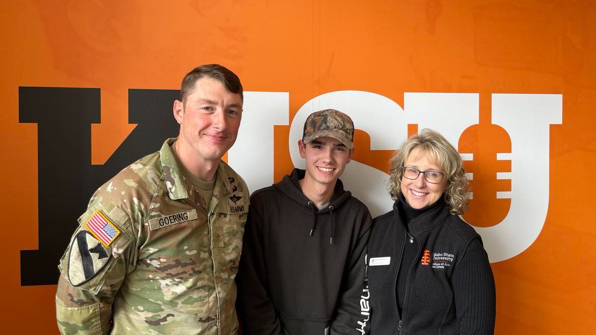 Goering, Storm, and Turley Ames stand together smiling for a picture with the orange KISU wall in the background