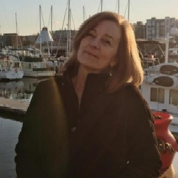 Mary standing on a dock with boats and masts in the background at sunset.