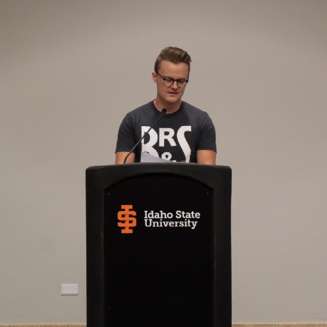 A student stands at a podium and reads his poem. 