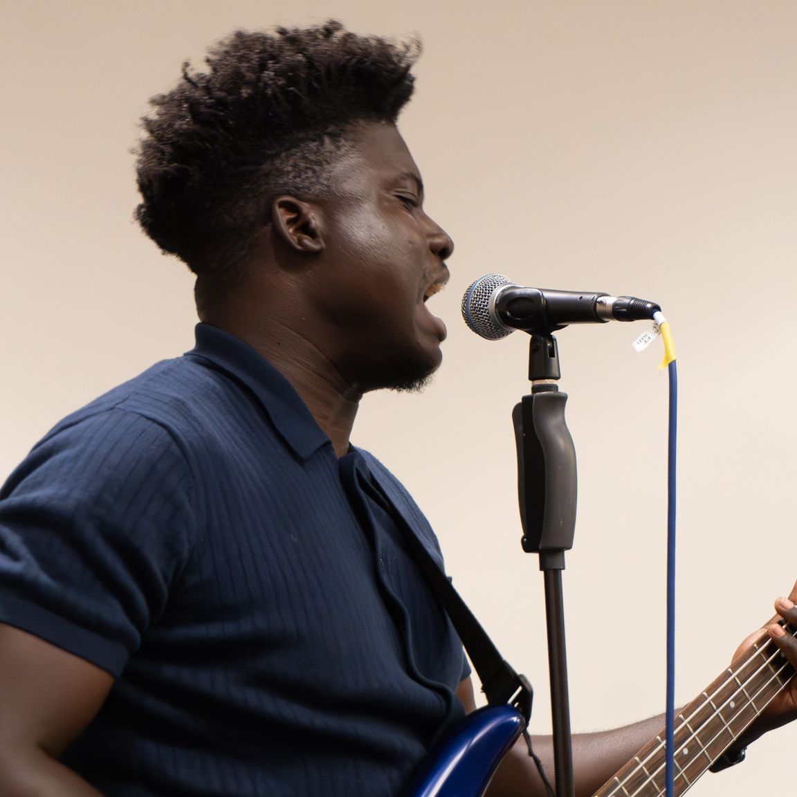 A student sings at a microphone and plays a blue electric guitar