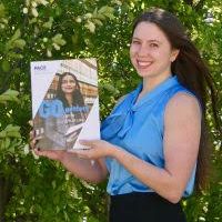 Ailie holds a copy of a publication. She stands outside next to a tree.