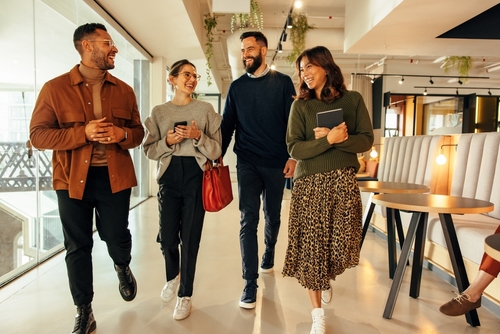 Young businesspeople walking through a modern office in the morning. Team of happy businesspeople smiling cheerfully. Group of diverse entrepreneurs working together in a co-working space.