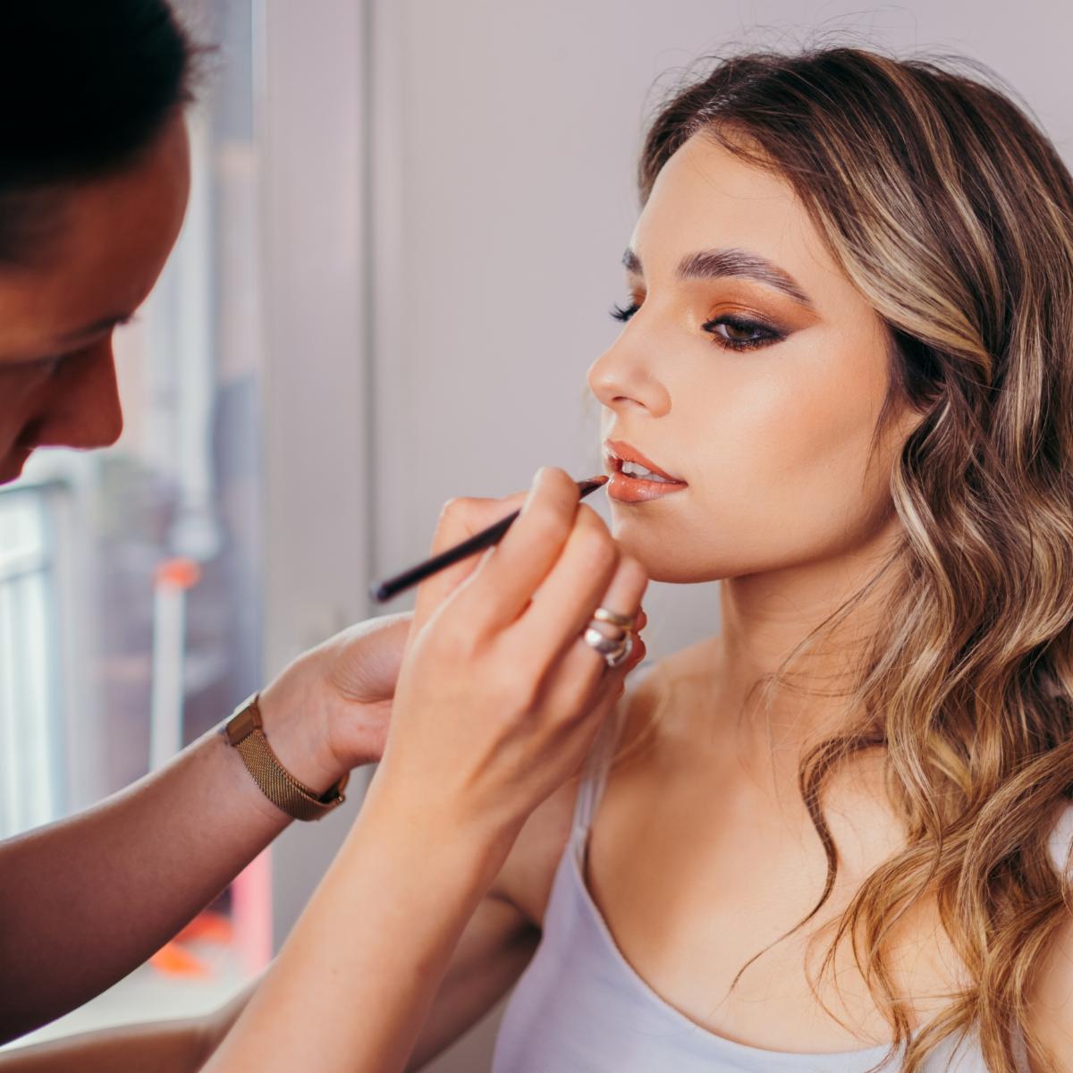 Female makeup artist applies rose lipstick. Beautiful females