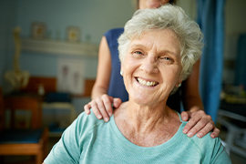 Woman smiling at the camera with another person's hands on her shoulder.