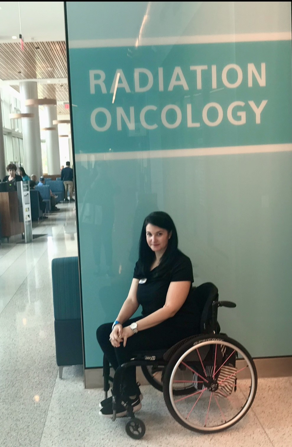 Photo of Justine in a wheelchair in front of a Radiation Oncology sign