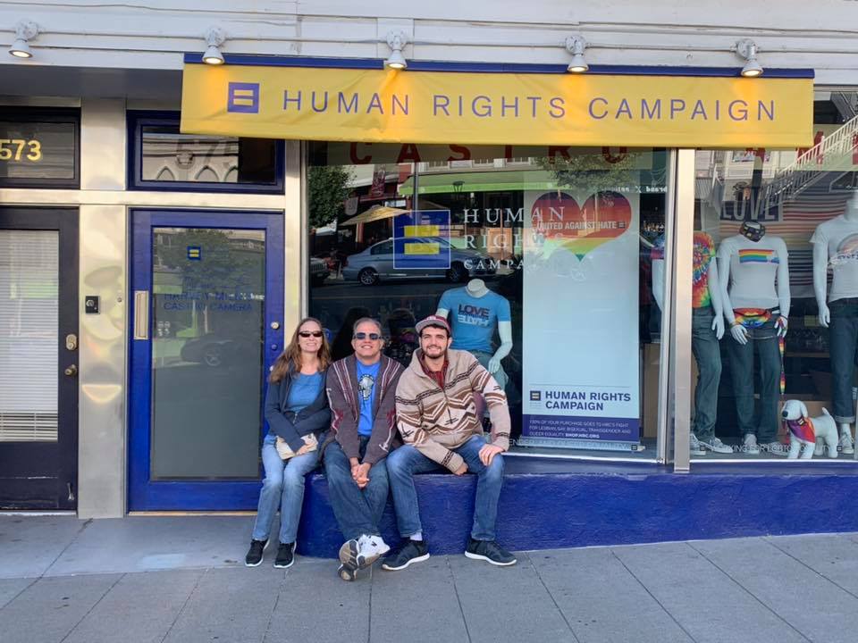 debbie matt and max sitting in front of a store front with a banner saying human rights campaign in the castro district of san francisco
