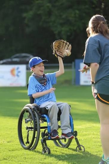 a little boy using a wheelchair playing baseball wearing a glove and catching a ball