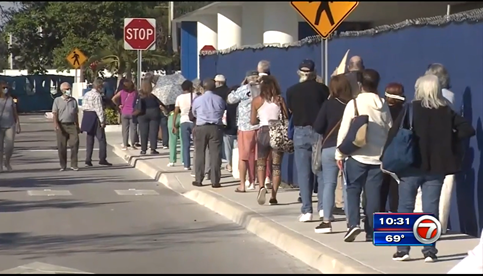 people standing in a line on the side of the street waiting for a COVID-19 vaccine