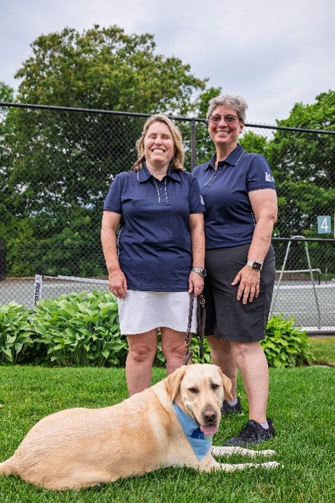 Megan and Ann smile at the camera while Woodstock lays in the grass in front of them.