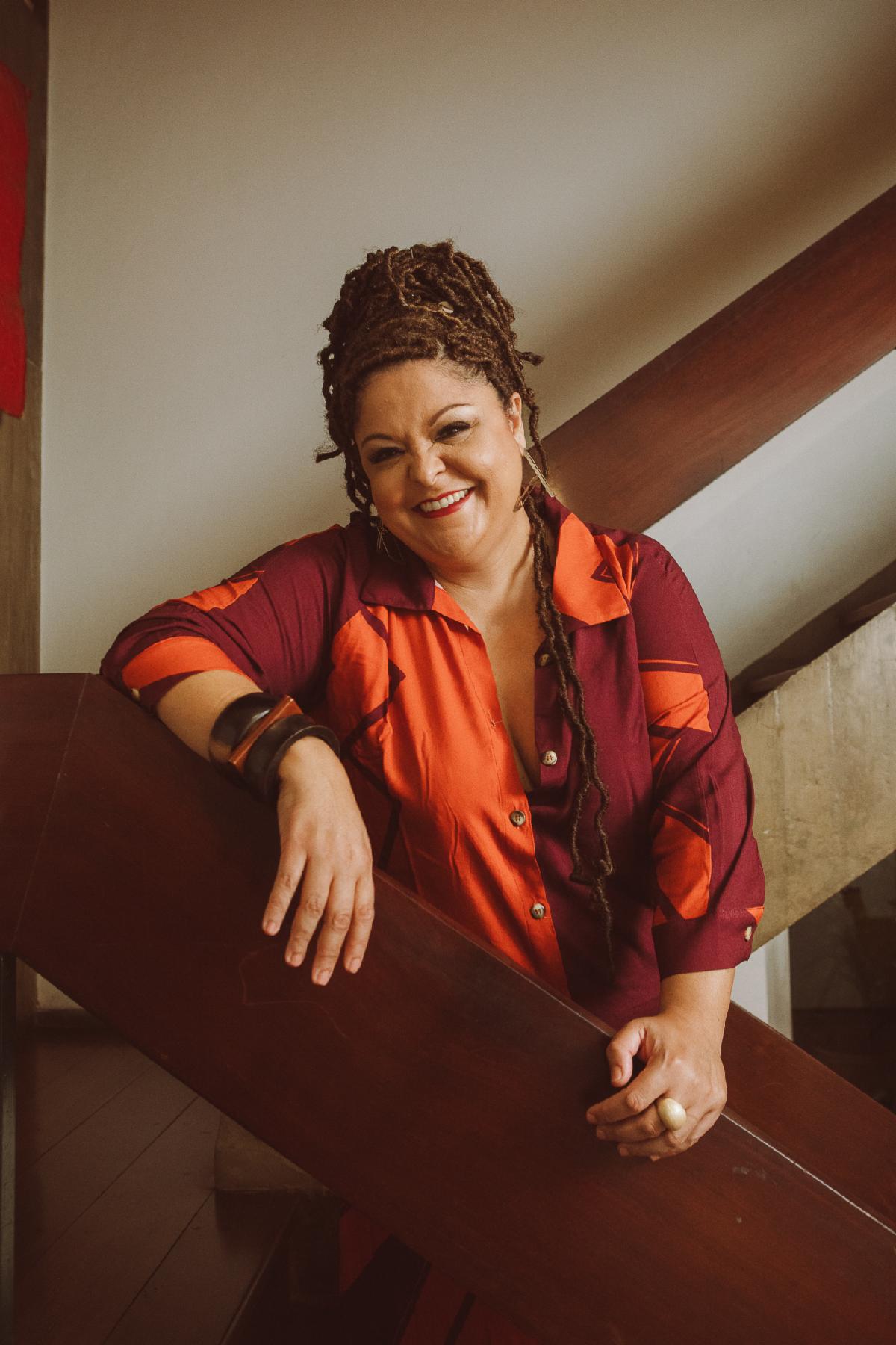 A woman smiles wearing a multipatterned red top