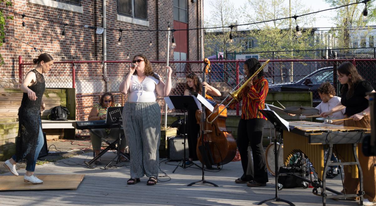 A group of women playing various instruments perform at an outdoor stage.