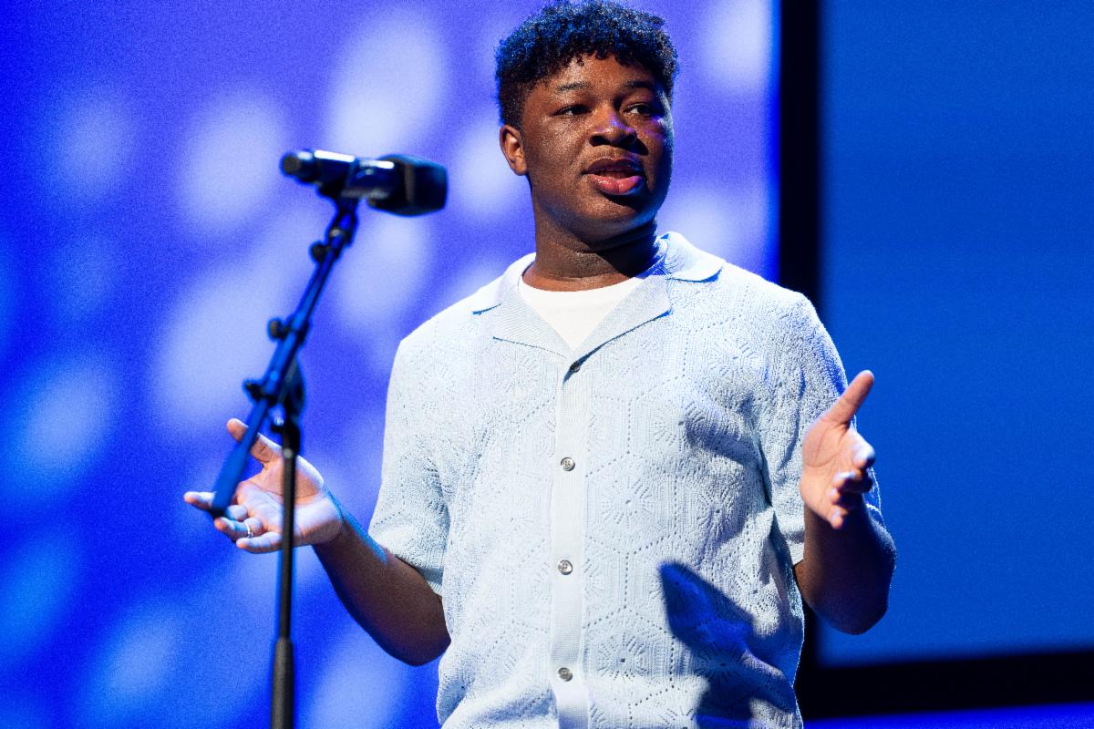 A teen boy in a blue button down shirt recites poetry at a microphone