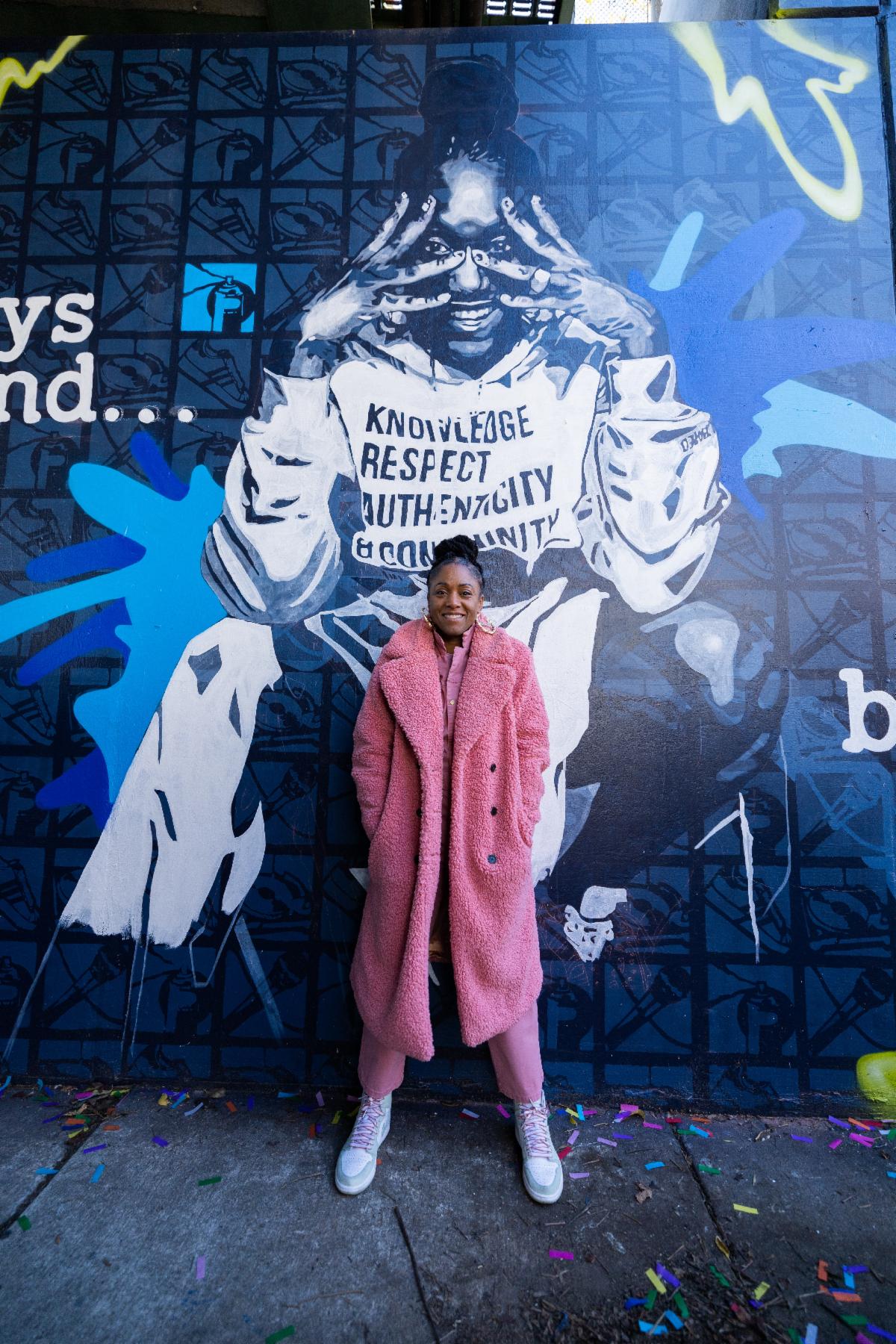 Michele Byrd-McPhee wears all pink and stands in front of a mural 