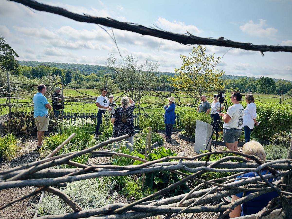A group of people stand outside in a garden for a talk.