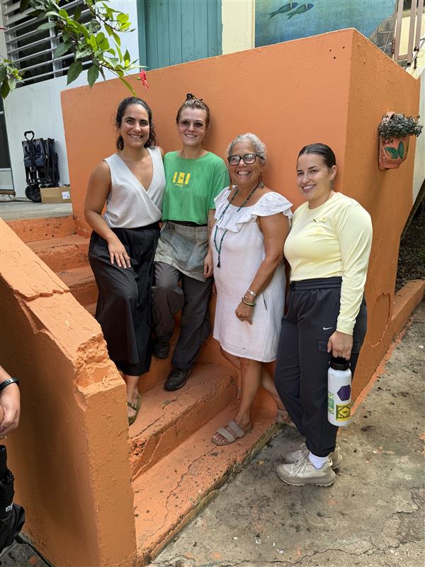 Four women stand in front of an orange wall