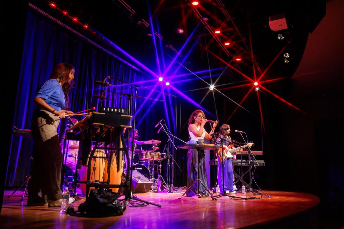 An ensemble of women sing on a stage with instruments around them