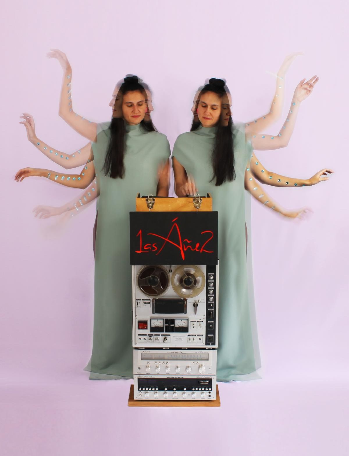 two women in light green floor length dresses stand side by side behind an old recording system