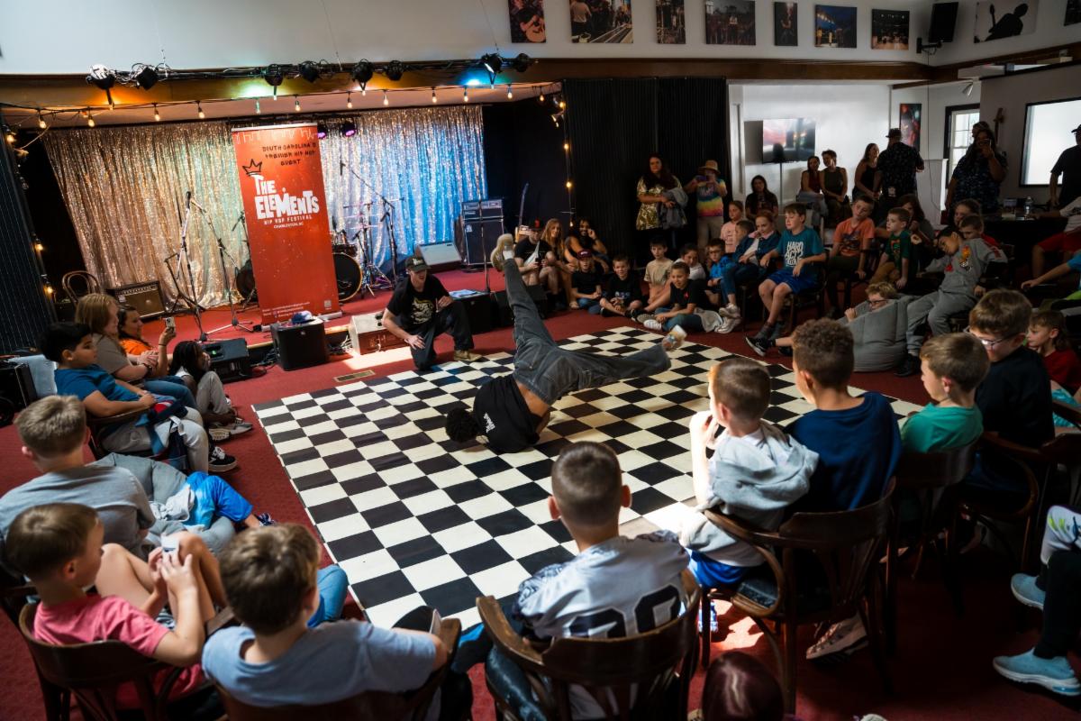 A breakdancer spins on a checkered floor in front of a circle of audience members