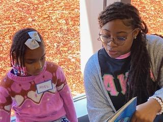 A photo of a college-aged woman reading a book to an elementary school student