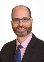 Bearded brunette man with glasses in suit and tie.