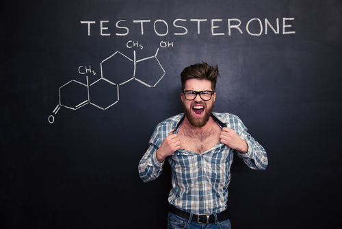 Aggressive young man in glasses screaming and tearing off his shirt over blackboard background
