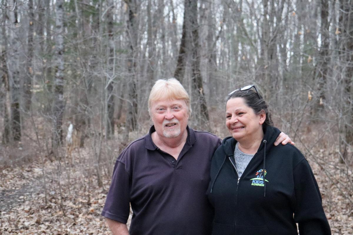 A man and woman stand in their wooded backyard