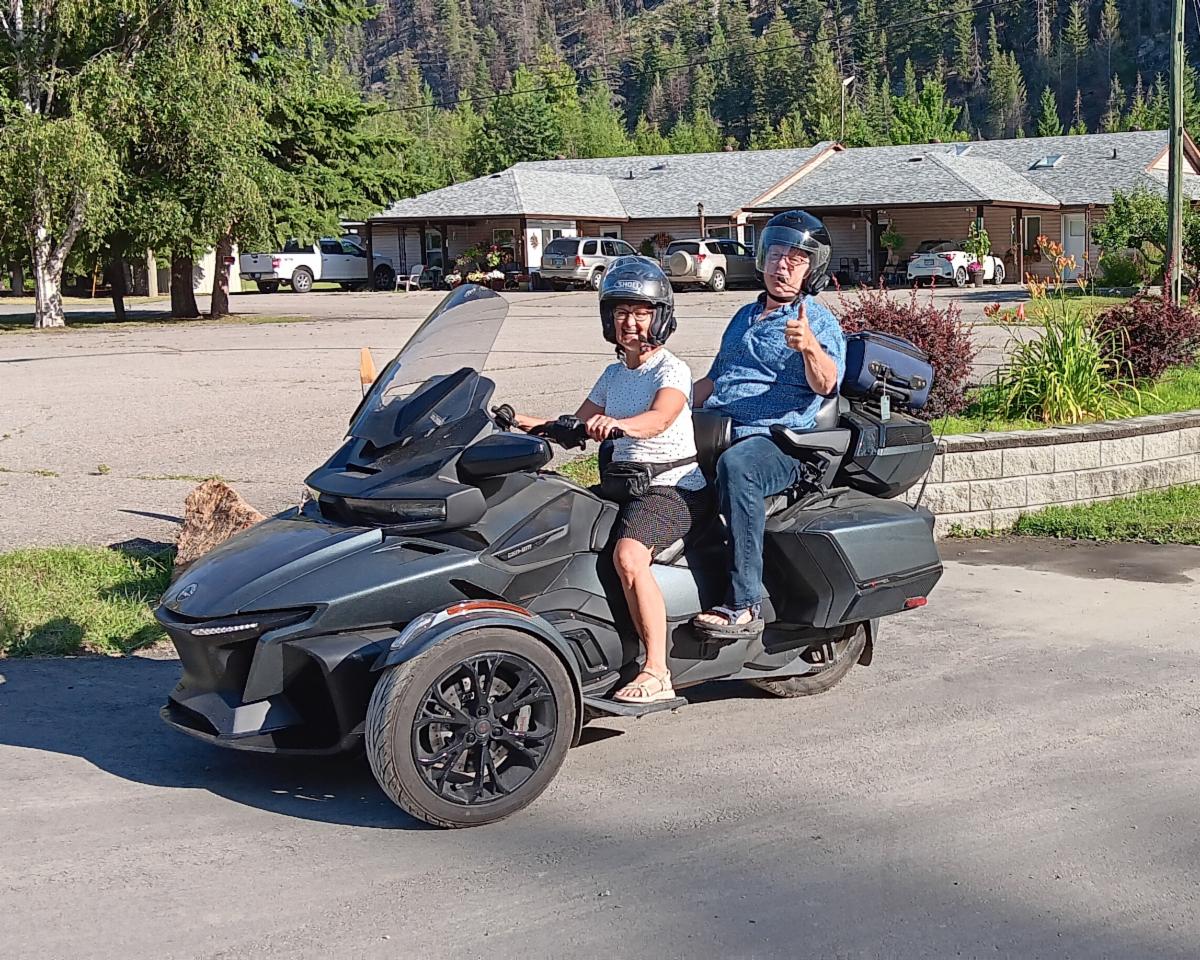 Two people sit on a three-wheeled motorbike