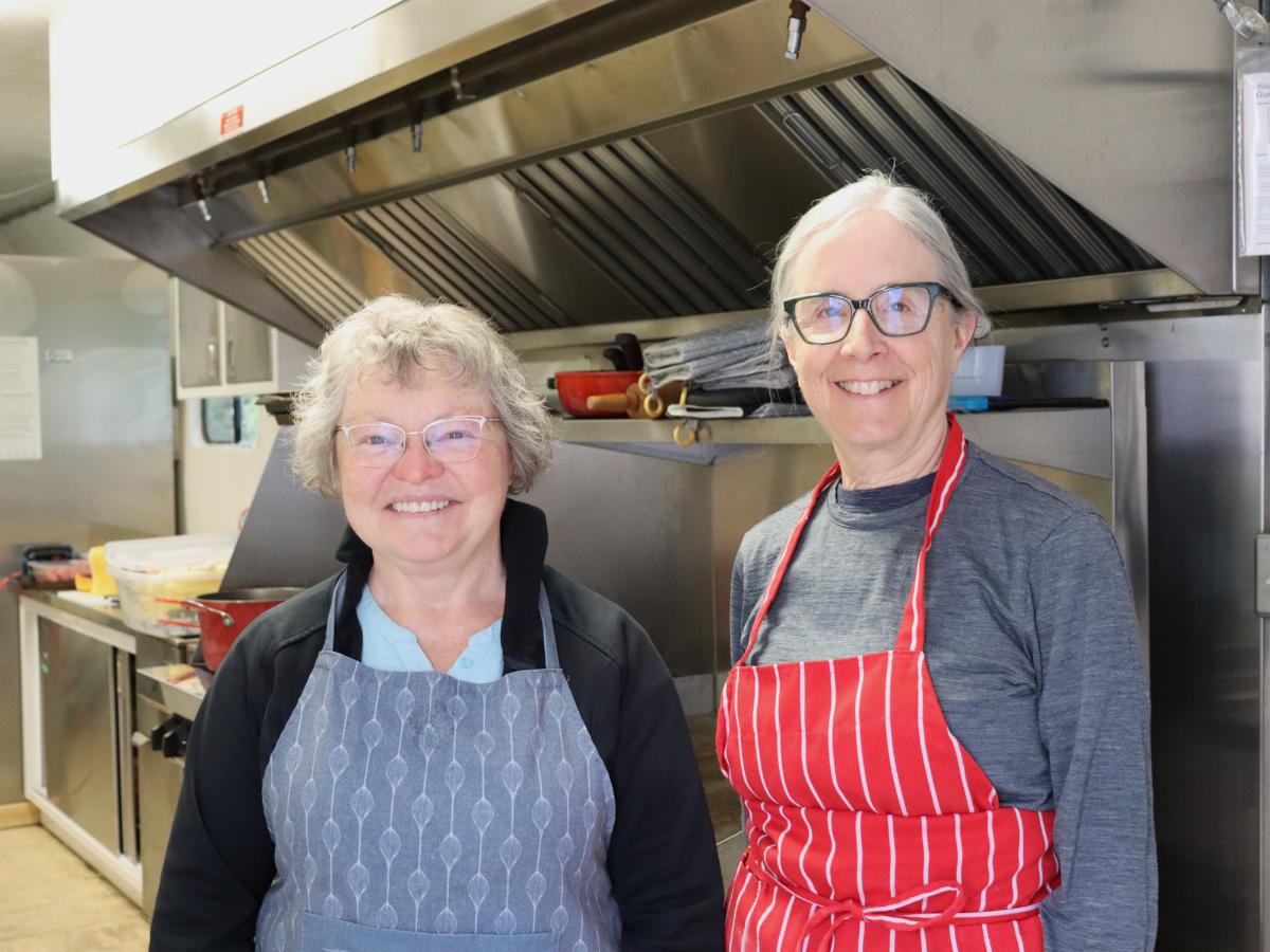 Two women in aprons stand in a kitchen trailer
