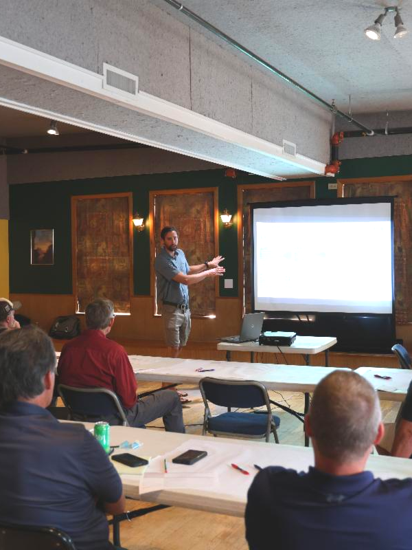 Agricultural Lead, Davis Clark, presents at a community meeting. People sit and watch, he points to a projector screen.