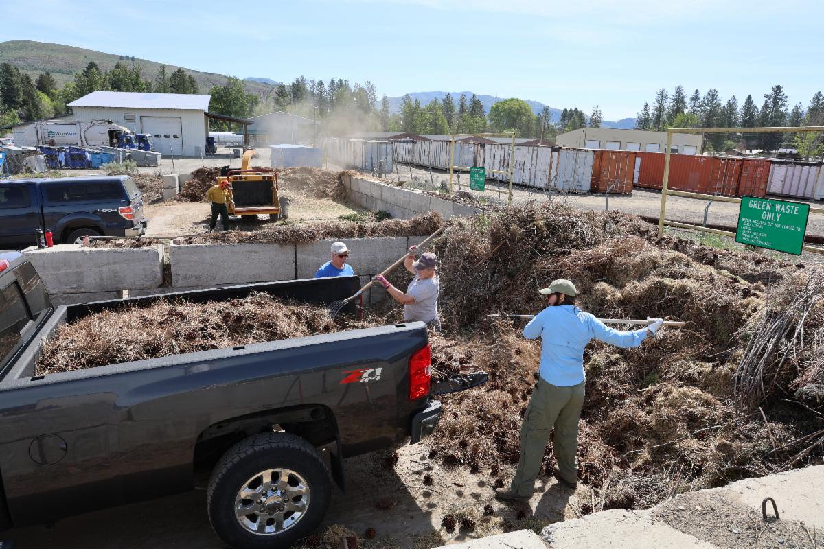 Okanogan CD staff assisting a landowner at the Twisp Transfer Station Chipping Event. Pictured in front of a huge pile of woody debris and actively scooping debris out of the back of a pick up truck.
