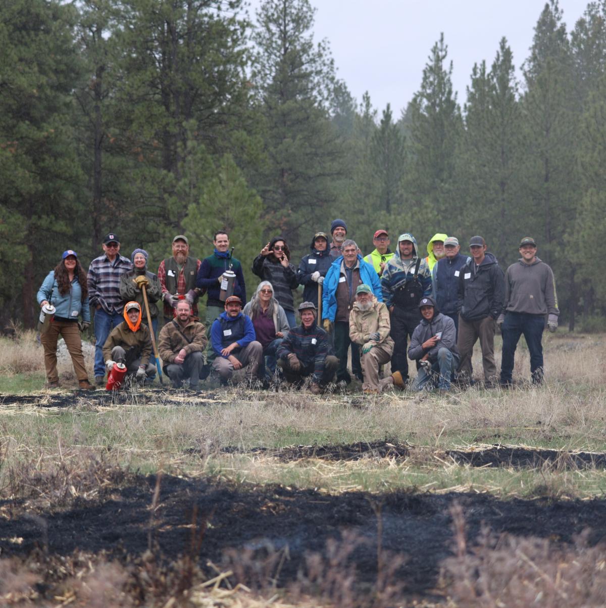 Group of 22 people at Learn to Burn event, smiling for a group photo in the woods.