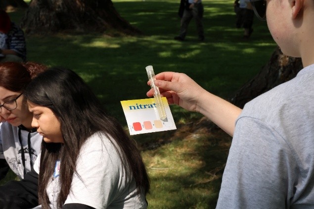 A student taking water quality measurements and holding a vile and paper to indicate nitrate levels.