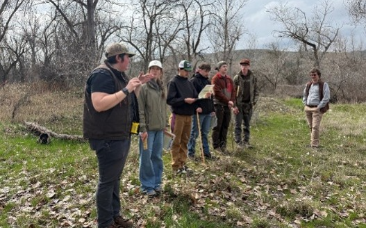 6 students pictured standing along river and listening as Okanogan CD staff leads forestry field day.
