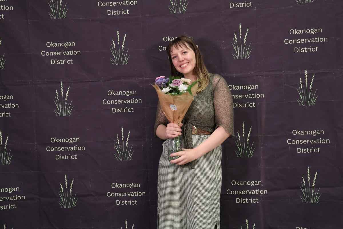 Rosalie Powell, Employee of the Year, holding flowers and smiling in front of backdrop.