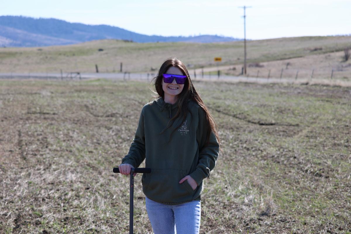 Previous staff member, Taylor George, standing in field with soil probe and smiling.