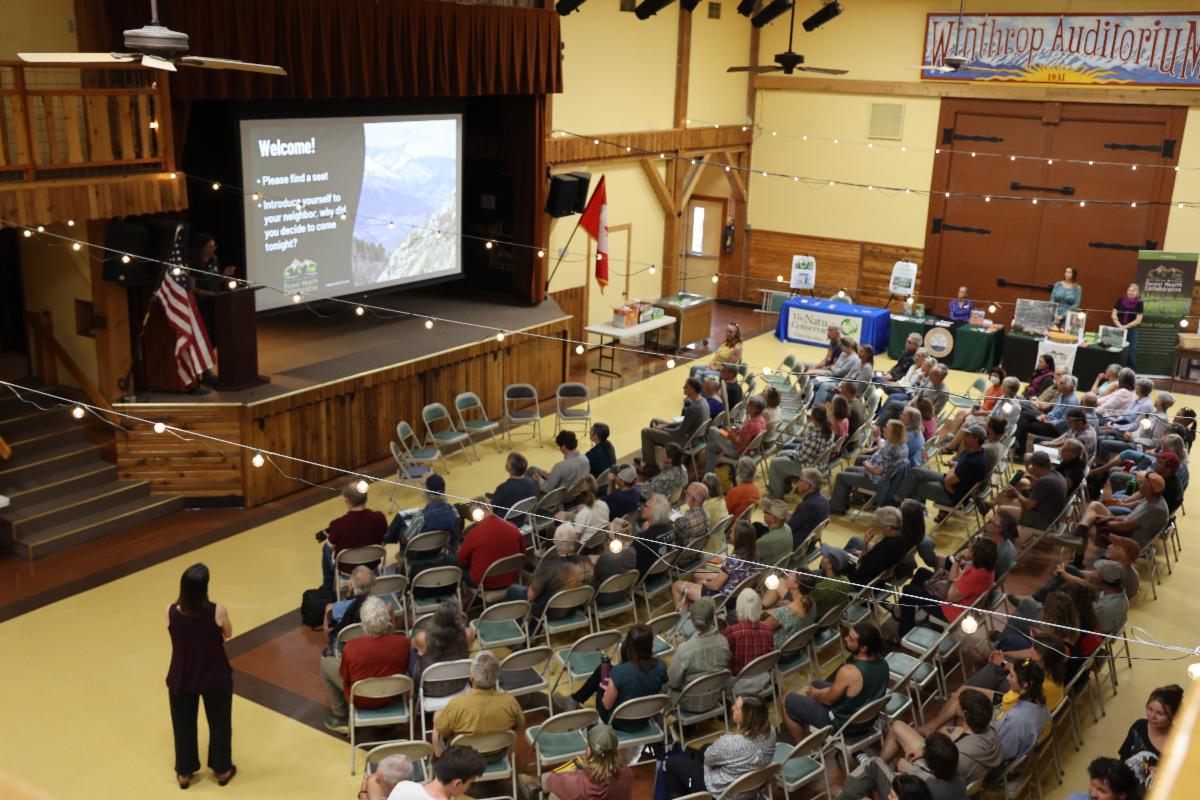 A photo taken from above showing a large group of people seated towards the stage, watching a presentation. 