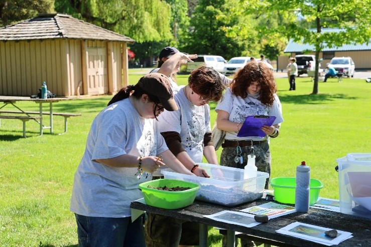 3 students working at a table with hands in a bucket to determine soil type.