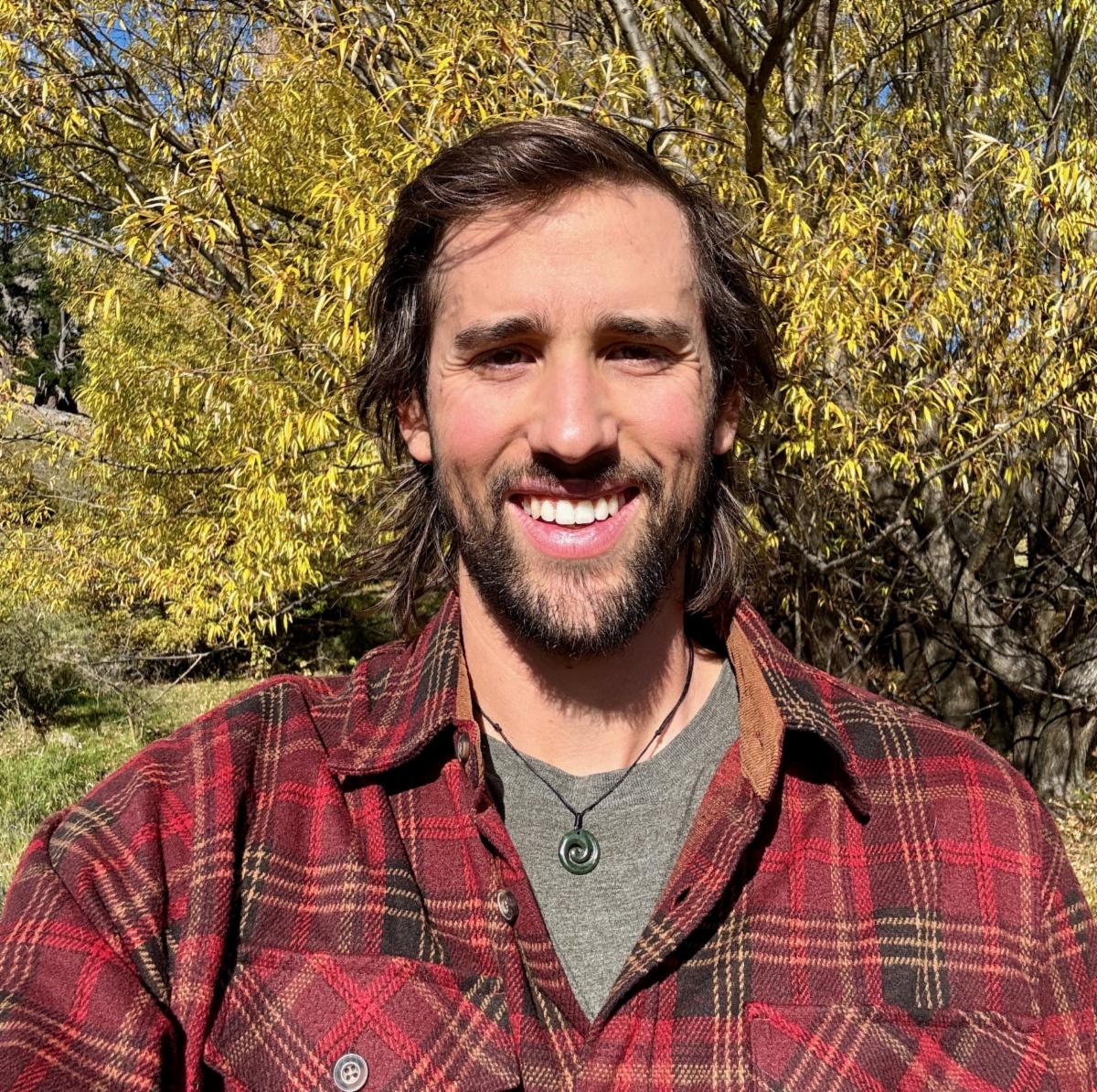 New staff member, Davis Clark, smiling and wearing a red flannel with yellow trees in the background