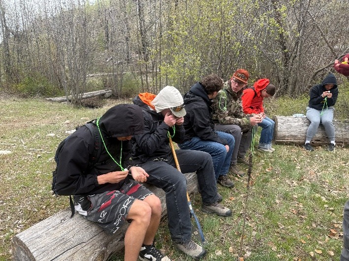 6 students sitting on a log looking at plant indicators.