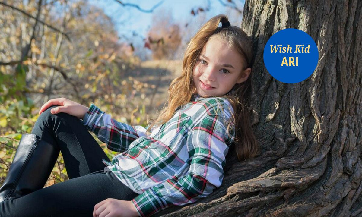 Wish Kid Ari leans against a tree and gives a sweet smile