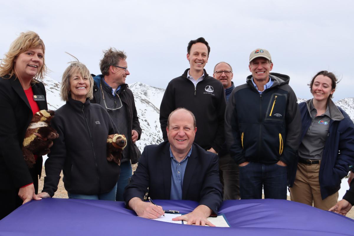 Governor Polis signs SB24-171 seated at a table on a mountain top.