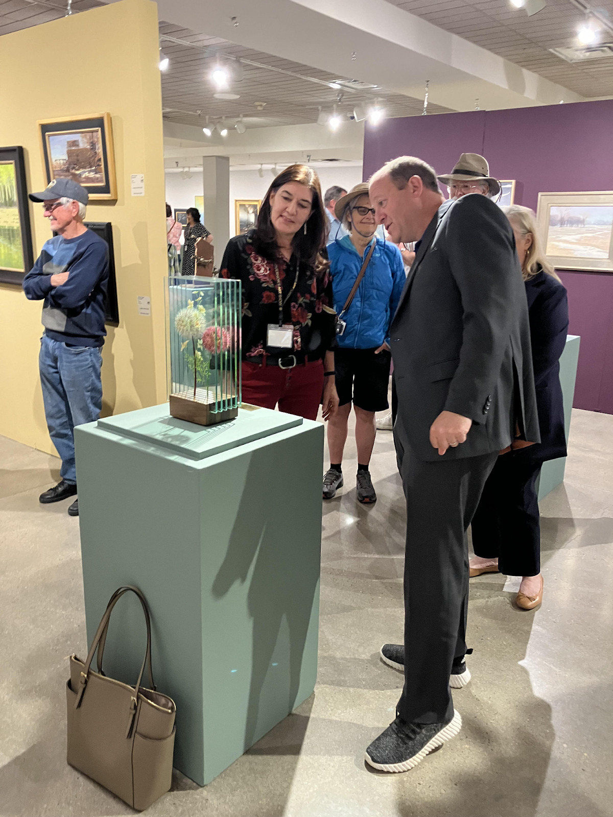 Governor Polis discusses a painting of flowers on glass with the local artist at the Governor's Art Show.