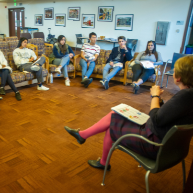 Multiple students from UC Davis sit in chairs facing a facilitator as part of a focus group