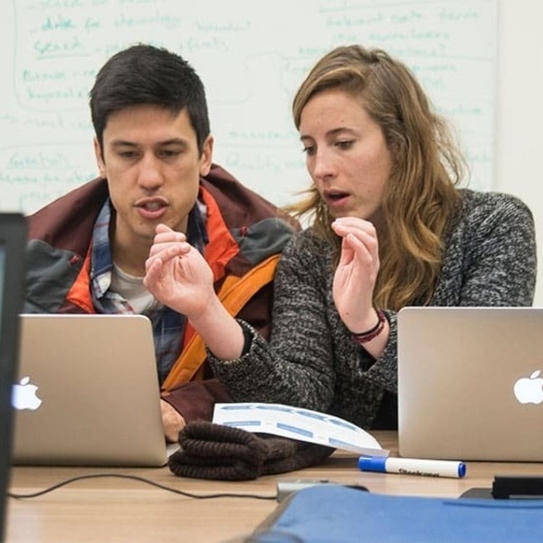 Two UC Davis students working together at a table with laptops discussing and pointing at the screen in a library setting