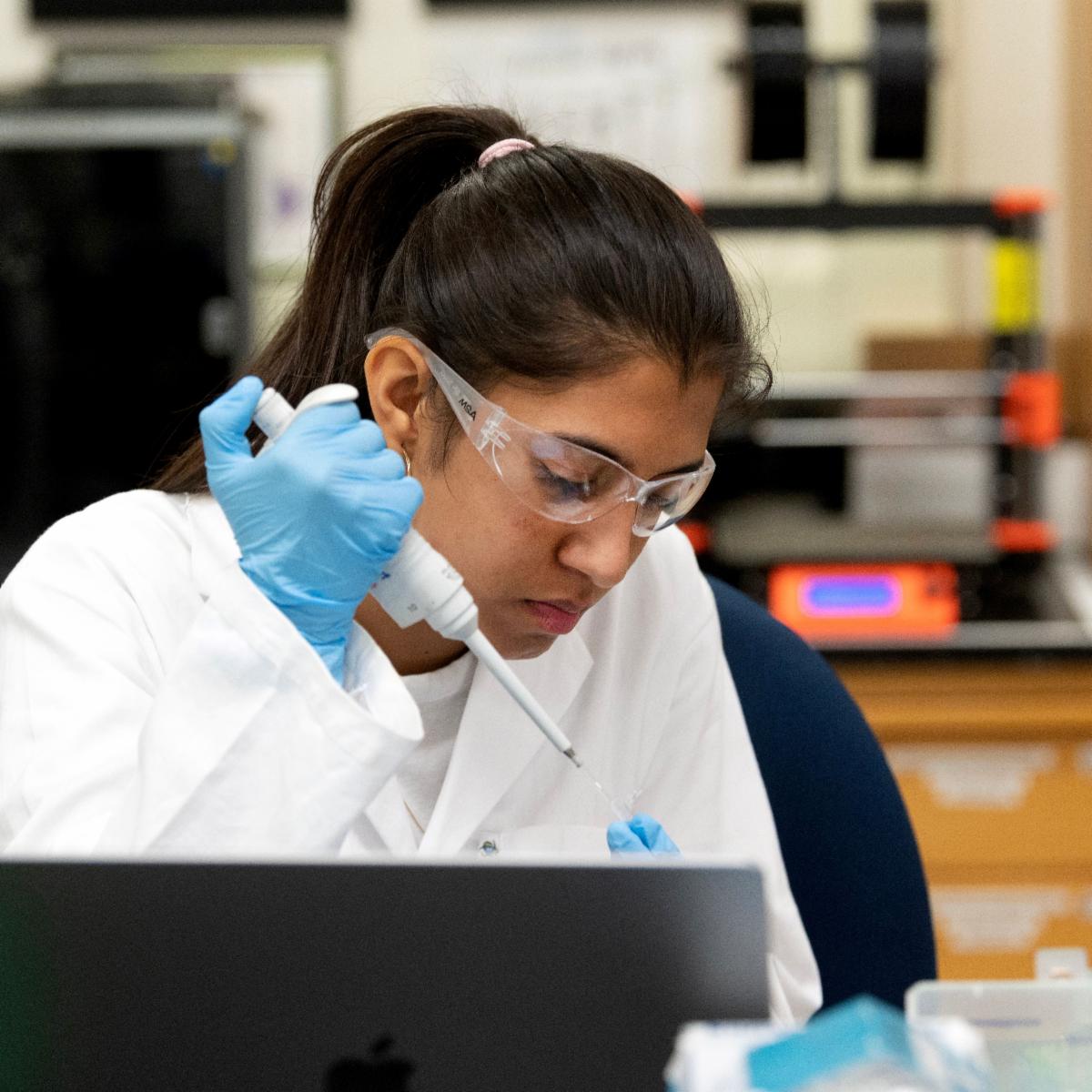 A CBS student wearing a lab coat conducts and experiment in a CURE course