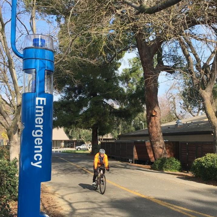 Image of a blue "Emergency" safety pole with a cyclist to the right on the UC Davis campus.