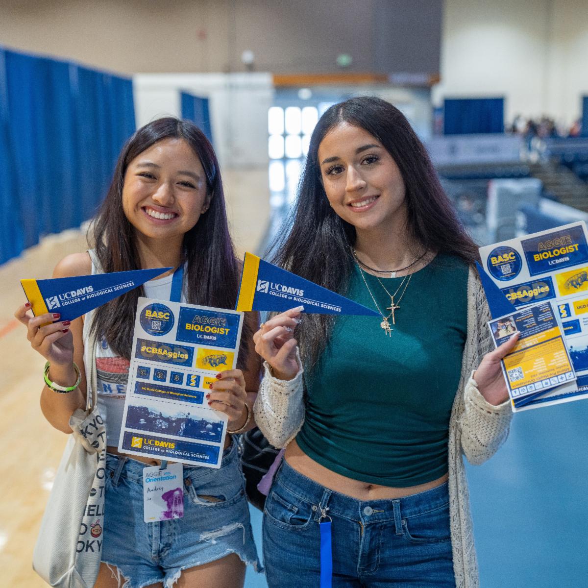 Two UC Davis College of Biological Sciences students smiling and holding CBS pennants and keyboard stickers during the college welcome event for the Class of 2029