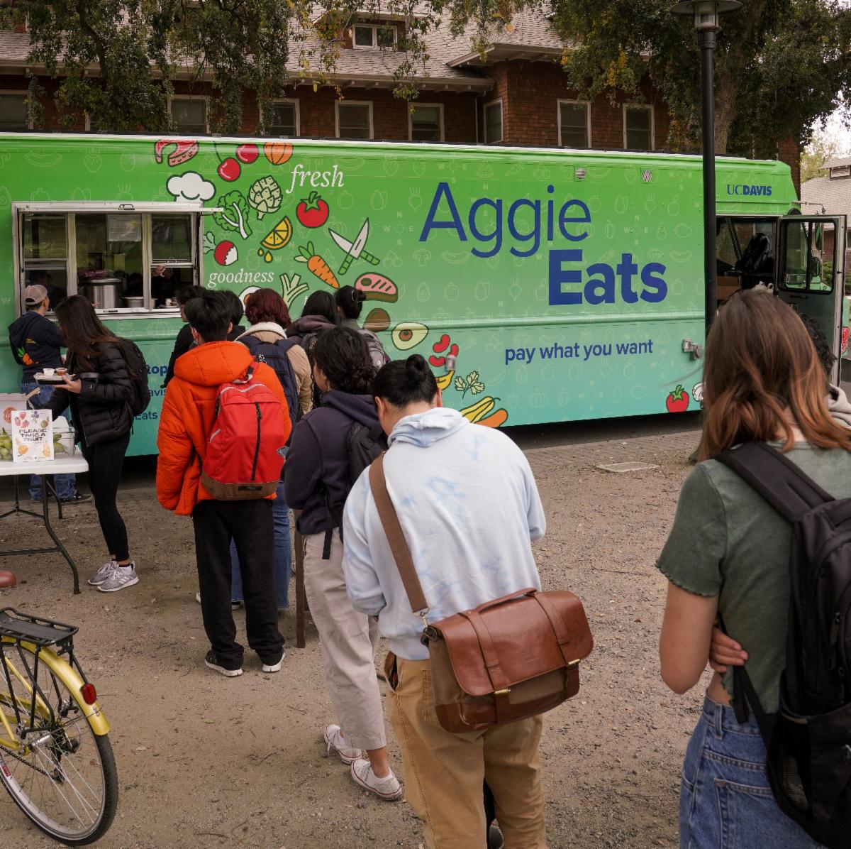 UC Davis students standing in line at the Aggie Eats food truck with a bright green design and pay what you want message