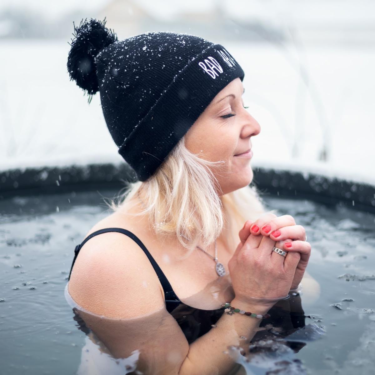 Image of a woman wearing a knitted hat and bathing suit while submerged in a cold plunge pool